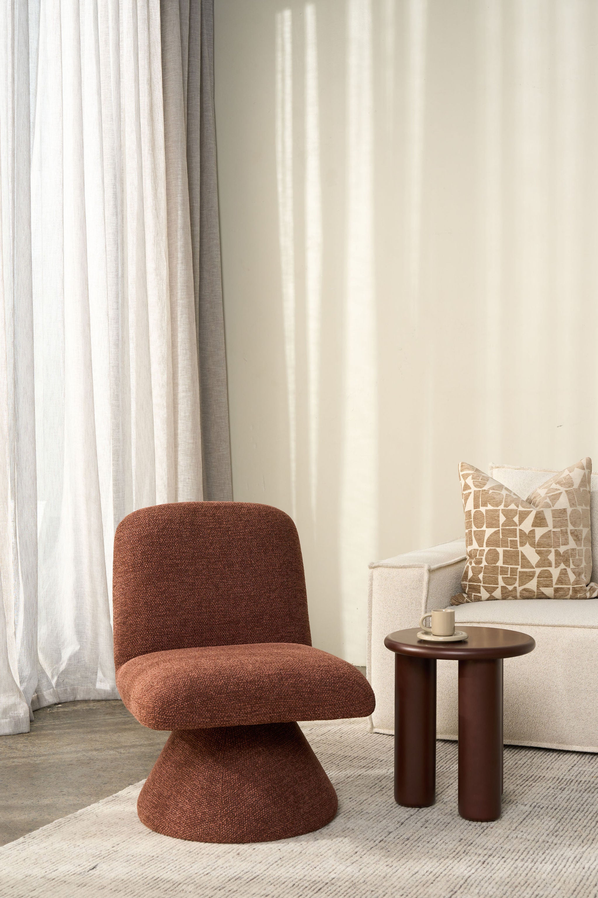 Brown chair and small table in a room with white curtains and a patterned pillow.